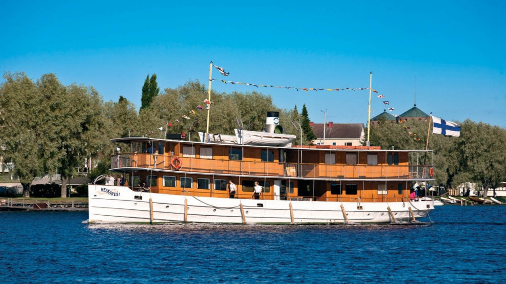 Koristein liputettu Saimaan Laivamatkojen S/S Heinävesi risteilee kirkkaalla järvellä kaupungin edustalla.