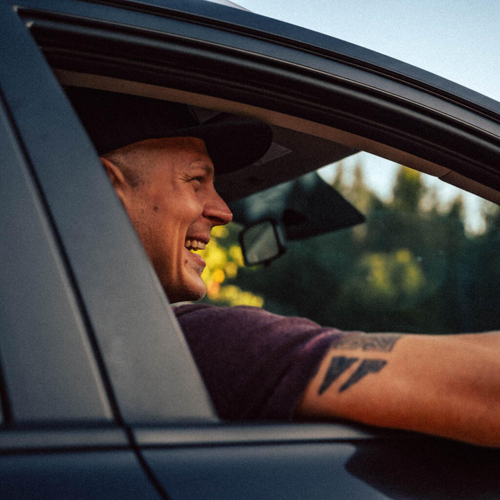 Hymyilevä henkilö istuu auton ratissa ikkuna auki.