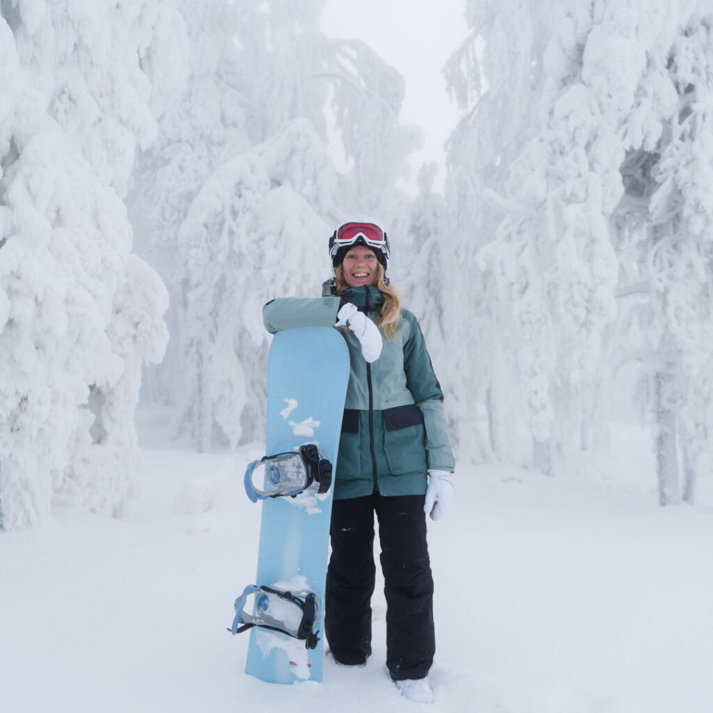 Tahko talvi, nainen seisoo lumilaudan kanssa tykkylumisten puiden edessä Tahkon rinteillä.